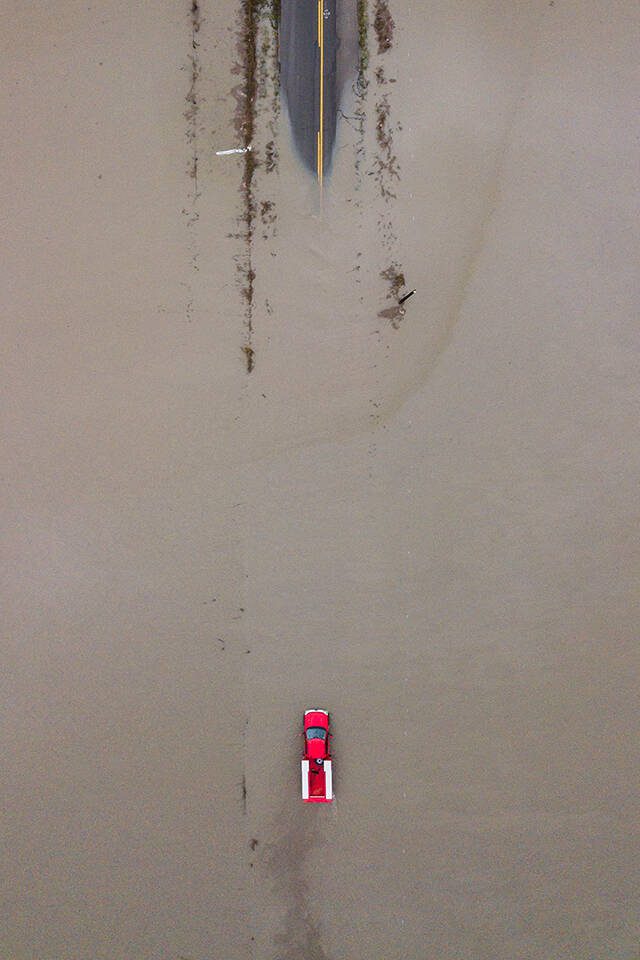 A red truck navigates through floodwaters covering 28th Avenue NW along Pioneer Highway on Wednesday, Dec. 6, 2023 in Stanwood, Washington. (Olivia Vanni / The Herald)