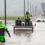 Snohomish County Sheriff Dive Team and Search and Rescue deputy William Dawson approach two men and two dogs sitting in the bed of their truck. The truck died while trying to cross floodwaters along 28th Avenue NW on Wednesday, Dec. 6, 2023, in Stanwood, Washington. (Olivia Vanni / The Herald)