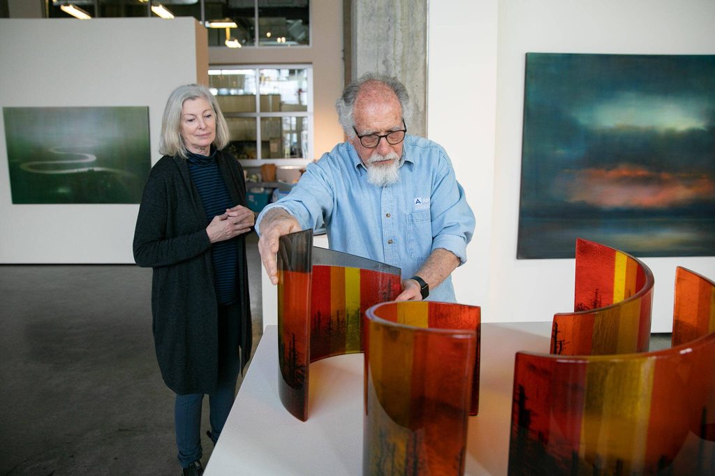 Steve Klein moves some of his glasswork into place as fellow guest curator Meg Holgate watches during installation of A Precarious Edge at Schack Art Center on Sunday, March 19, 2023, in Everett, Washington. (Ryan Berry / The Herald)