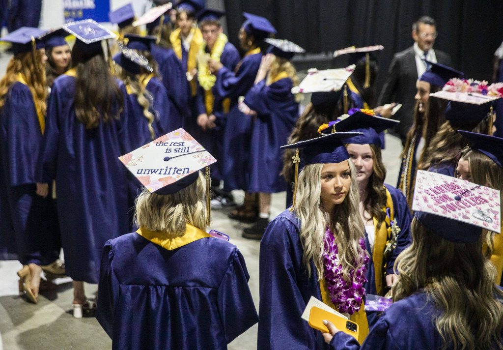 Students gather with decorated graduation caps before the start of Arlington High School graduation at Angel of the Winds Arena on Thursday, June 13, 2024, in Everett, Washington. (Olivia Vanni / The Herald)