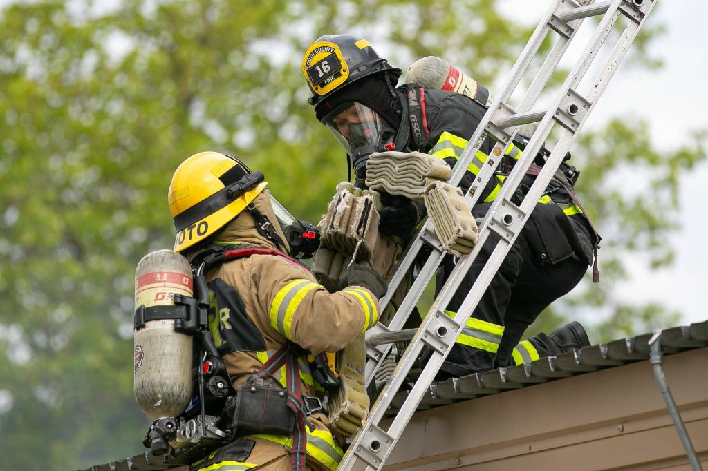 Two South County firefighters rescue a dummy from the second floor of a burning building during a simulation at the Future Women in EMS/Fire Workshop on Saturday, June 22, 2024, at the South County Fire Training Center in Everett, Washington. (Ryan Berry / The Herald)
