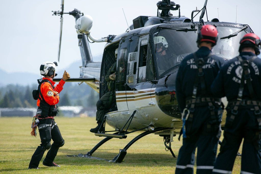 HRT Rescue Technician Andy Toyota gives the thumbs-up to crew members in the Snohomish County Volunteer Search and Rescue helicopter shortly before takeoff during an interagency training session held by Northwest Regional Aviation on Thursday, June 13, 2024, at the Arlington Airport in Arlington, Washington. (Ryan Berry / The Herald)