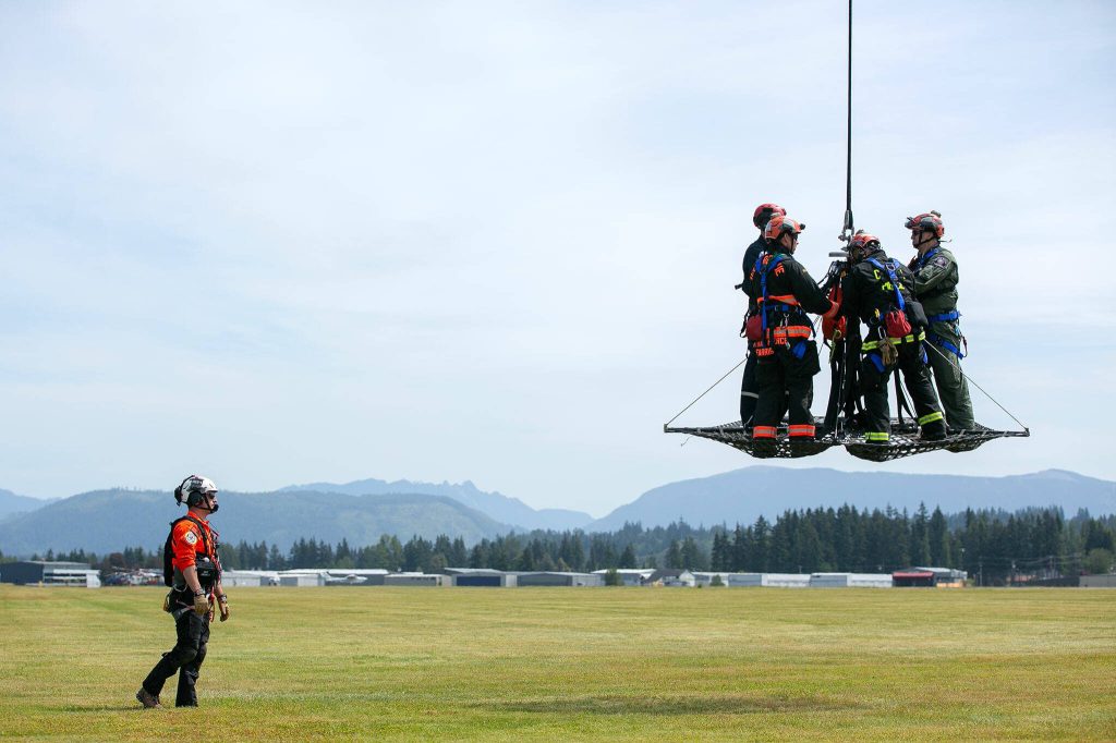 Snohomish County Volunteer Search and Rescue Flight Medic Jeff Brown, left, watches as a crew of volunteers take flight in an AirTEP being lifted by a helicopter during an interagency training session held by Northwest Regional Aviation on Thursday, June 13, 2024, at the Arlington Airport in Arlington, Washington. (Ryan Berry / The Herald)