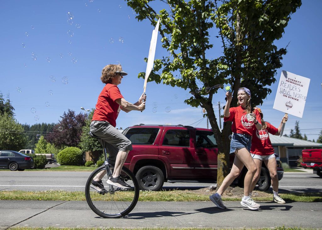 Olivia Vanni / The Herald
Jenelle Baumbach, right, runs ahead of Janice Podsada, left, with a bubble gun as Podsada rides her unicycle down the sidewalk along Colby Avenue during the second day of the Everett NewsGuilds strike on Tuesday, June 25, 2024 in Everett, Washington.