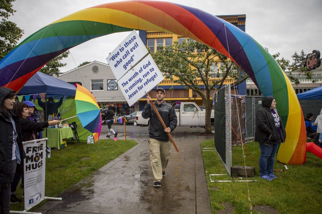 A protestor walks under a rainbow arch during the third annual Arlington Pride event in Arlington, Washington on Sunday, June 2, 2024. (Annie Barker / The Herald)