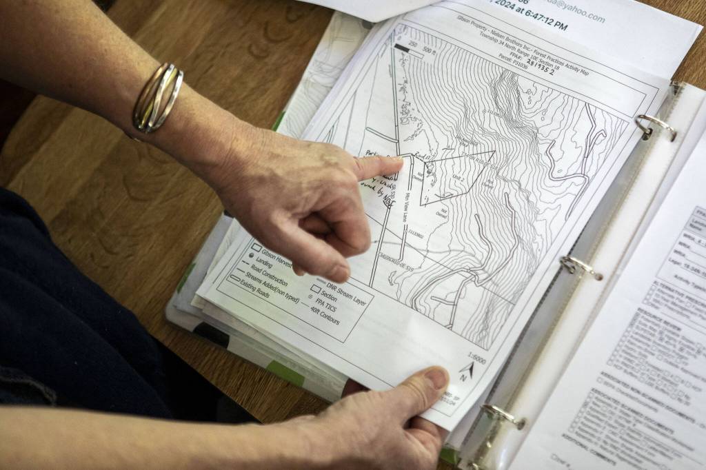 Kim Skarda points at her home on a map on Thursday, June 20, 2024 in Concrete, Washington. A community called Sauk River Estates has a very steep slope above it. There is a DNR-approved timber sale that borders the estate properties, yet they were not consulted about the sale before approval. The community has already appealed the sale and has hired their own geologist to conduct a slope stability report at the site. (Annie Barker / The Herald)
