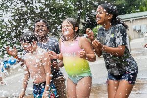 Oliver Fitting, 8, (left to right) Armon Desta, 11, and Capri Fitting, 9, and Hermela Desta, 12, close their eyes and brace for a large rush of water to be dumped on them at Hazel Miller Spray Park on Wednesday, June 26, 2024 in Edmonds, Washington. (Olivia Vanni / The Herald)