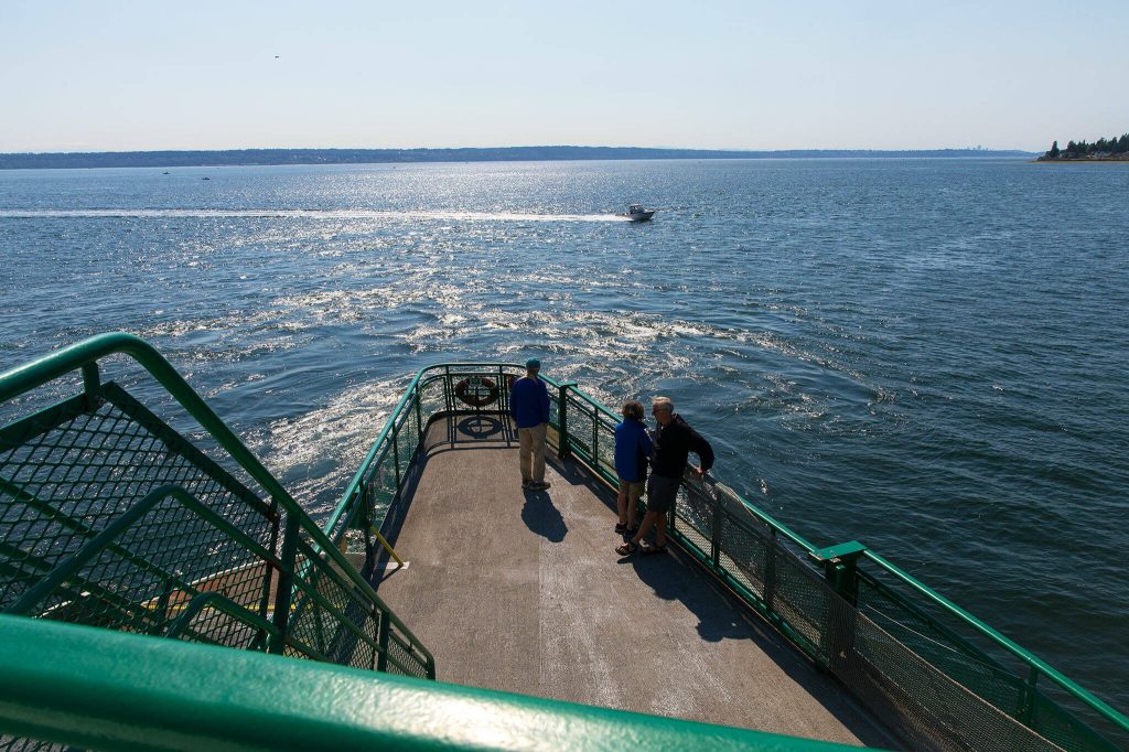 Travelers watch a boat pass in front of the MV Spokane as it departs the Kingston terminal on Thursday, July 18, 2024, near Kingston, Washington. (Ryan Berry / The Herald)