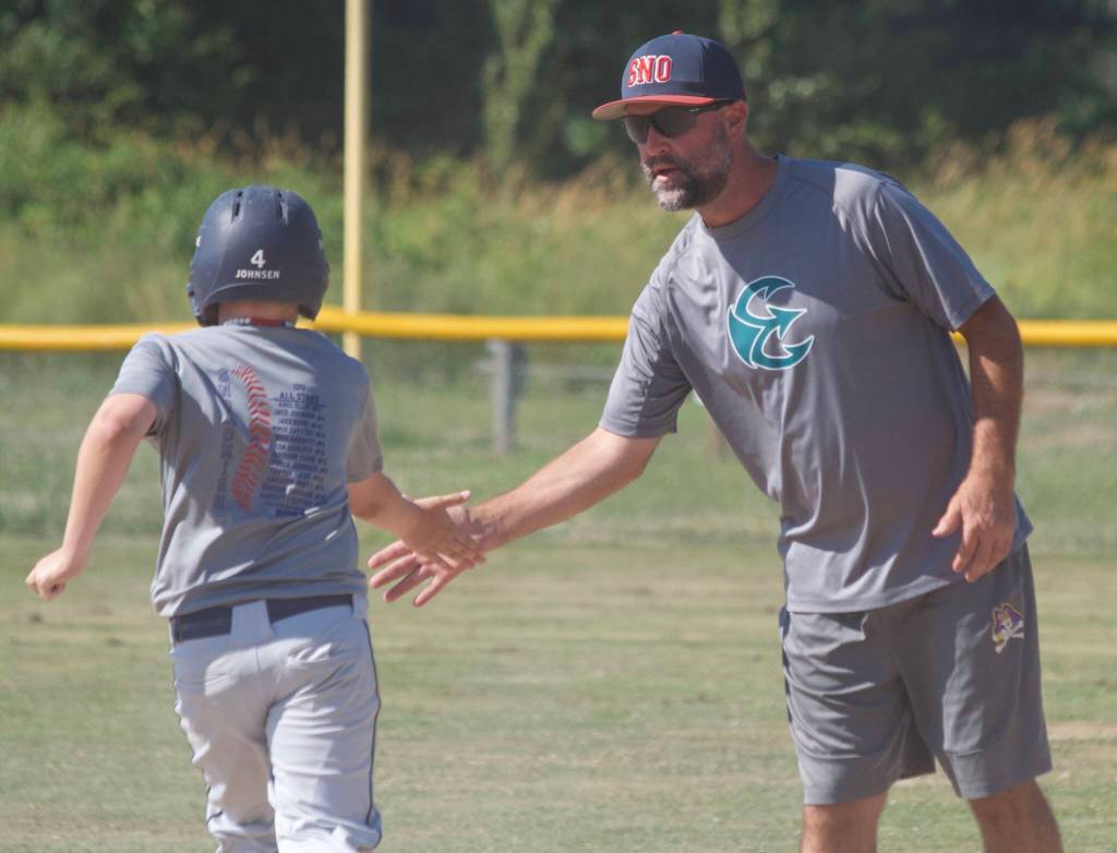 Boys Snohomish Little League 8-10 coach Aaron Barstad high fives Jace Johnsen during base-running training at the Snohomish Little League Complex in Snohomish, Washington on Thursday, July 18, 2024. (Taras McCurdie / The Herald)