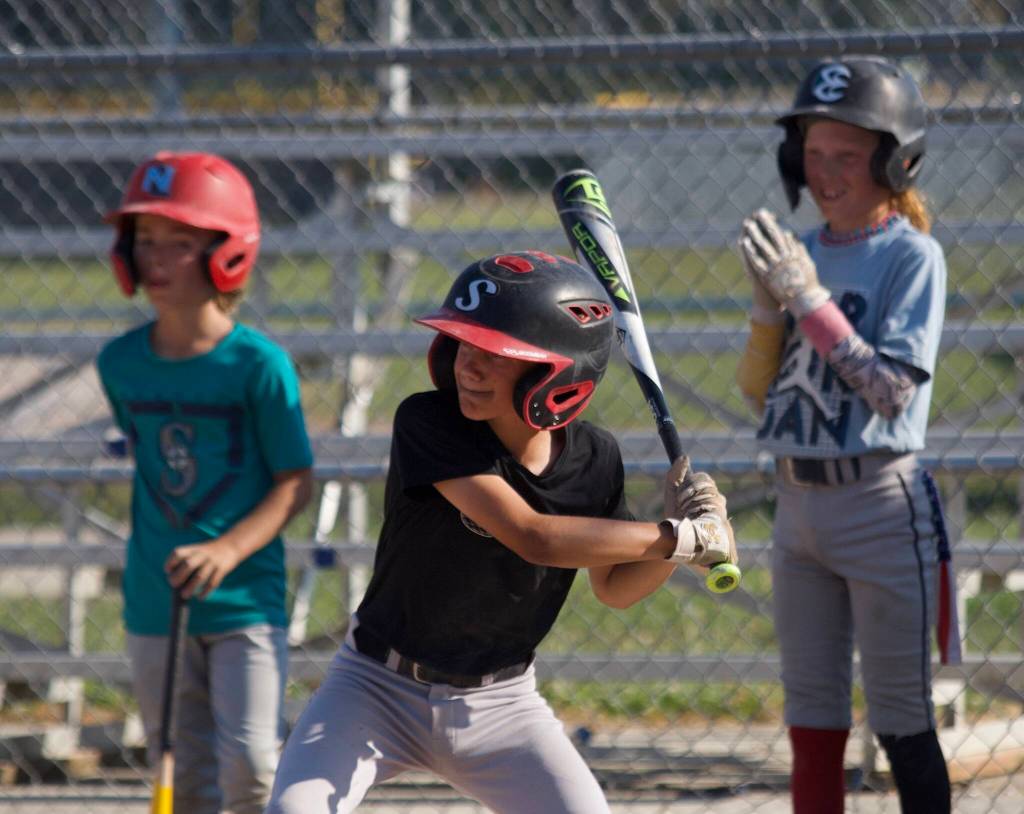 Will Garrett prepares to swing for the ball while Carter Bales (left) and Knox Barstad (right) observe during practice at the Snohomish Little League Complex in Snohomish, Washington on Thursday, July 18, 2024. (Taras McCurdie / The Herald)