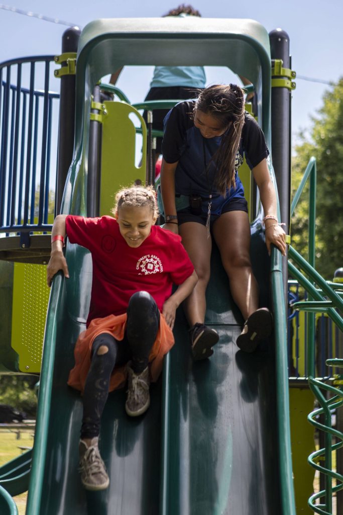 Amilya Mi Mi Plakio, 10, left, goes down a slide with counselor Yi Thomsen, right, during Camp Prov at Forest Park in Everett, Washington on Wednesday, July 24, 2024. (Annie Barker / The Herald)