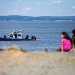 People watch an Everett Police boat from Edgewater Beach search for a missing kayaker on Monday, Aug. 19, 2024, in Mukilteo, Washington. (Olivia Vanni / The Herald)
