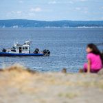 People watch an Everett Police boat from Edgewater Beach as they continue to search for a kayaker that went missing after a storm on Sunday on Monday, Aug. 19, 2024 in Mukilteo, Washington. (Olivia Vanni / The Herald)