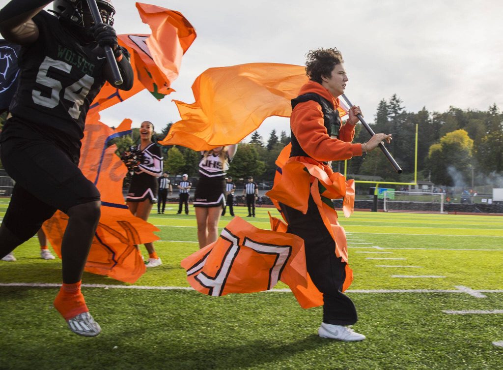 Will Turpin holds an orange flag and rips through a poster with his team during their orange out game for leukemia awareness on Friday, Sept. 20, 2024 in Everett, Washington. (Olivia Vanni / The Herald)