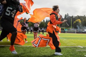 Will Turpin holds an orange flag and rips through a poster with his team during their “orange out” game for leukemia awareness on Friday, Sept. 20, 2024 in Everett, Washington. (Olivia Vanni / The Herald)