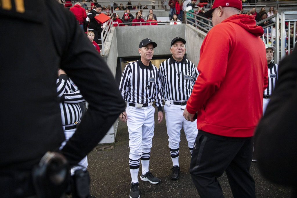 Steve Jensen and Dean Corcoran joke with coaches before the start of the football game on Friday, Oct. 4, 2024 in Snohomish, Washington. (Olivia Vanni / The Herald)