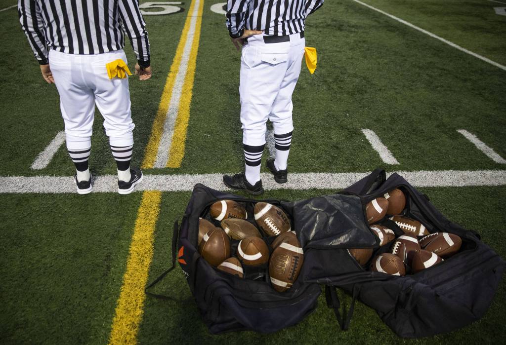 Yellow flags stick out of the back pockets of Ross Noe and Dean Corcoran as they wait on the 50-yard line for team captains before the start of the football game on Friday, Oct. 4, 2024 in Snohomish, Washington. (Olivia Vanni / The Herald)