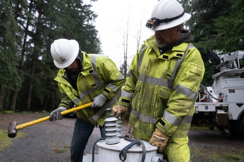 Drew Windsor, left, hits a transformer while Bryan Tugaw, right, holds it on Friday, Nov. 22, 2024, outside of Lake Stevens, Washington. The two are from Okanogan County. (Will Geschke / The Herald)