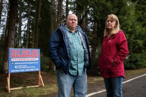 35th Avenue neighborhood residents John Ray, left, and Shelia Davis, right, next to one of many signs scattered throughout the neighborhood look for community support on Friday, Dec. 20, 2024 in Marysville, Washington. (Olivia Vanni / The Herald)