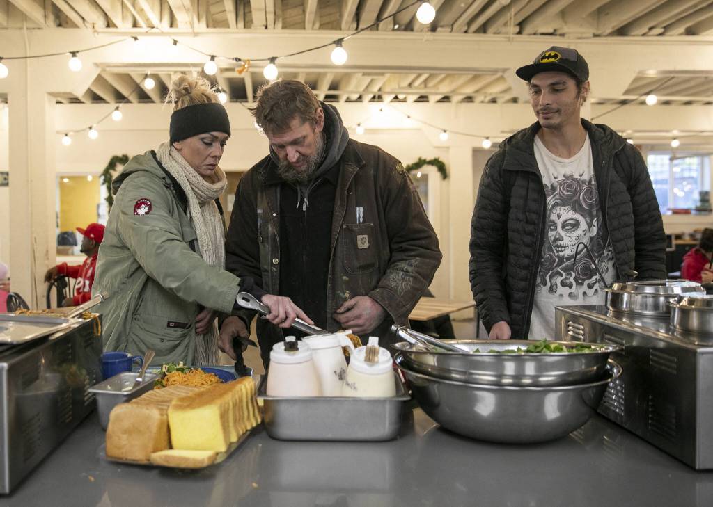 Carli Wiley, left, and Don Wiley, center, grab some of the homemade pasta during lunch at Everett Recovery Cafe on Wednesday, Dec. 4, 2024 in Everett, Washington. (Olivia Vanni / The Herald)