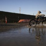 The Nosov family rides their bikes through a large puddle that formed next to the large piles of fill dirt at the Port of Everett on Monday, Dec. 9, 2024 in Everett, Washington. (Olivia Vanni / The Herald)