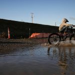 The Nosov family rides their bikes through a large puddle that formed next to the large piles of fill dirt at the Port of Everett on Monday, Dec. 9, 2024 in Everett, Washington. (Olivia Vanni / The Herald)