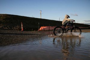 The Nosov family rides their bikes through a large puddle that formed next to the large piles of fill dirt at the Port of Everett on Monday, Dec. 9, 2024 in Everett, Washington. (Olivia Vanni / The Herald)