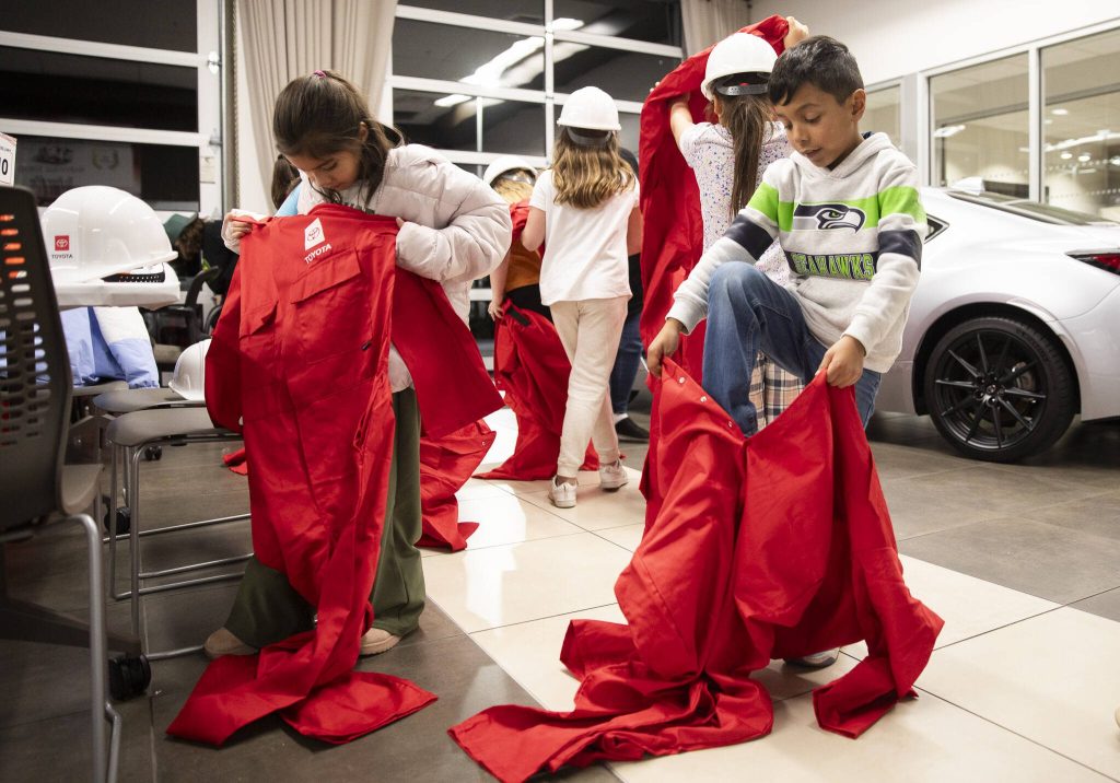 Elizabeth Gonzales, 8, left, and Lucas Rodriguez Hatch, 8, right, put on their oversized jumpsuits before the start of Toyota Mini Makers Garage on Monday, Dec. 9, 2024 in Marysville, Washington. (Olivia Vanni / The Herald)