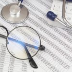 Stethoscope, glasses and calculator on financial documents close up.