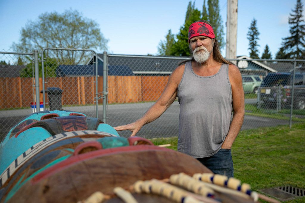 Tlingit artist Fred Fulmer stands over one of his completed totem poles while speaking about it on Wednesday, May 8, 2024, in the back yard of his home in Everett, Washington. (Ryan Berry / The Herald)