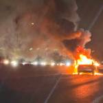 Two people stand on the highway as a car burns in the southbound lanes of Interstate 5 on Monday, Dec. 30 near Mountlake Terrace, Washington. (Eliza Aronson / The Herald)