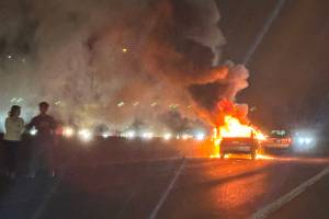 Two people stand on the highway as a car burns in the southbound lanes of Interstate 5 on Monday, Dec. 30 near Mountlake Terrace, Washington. (Eliza Aronson / The Herald)