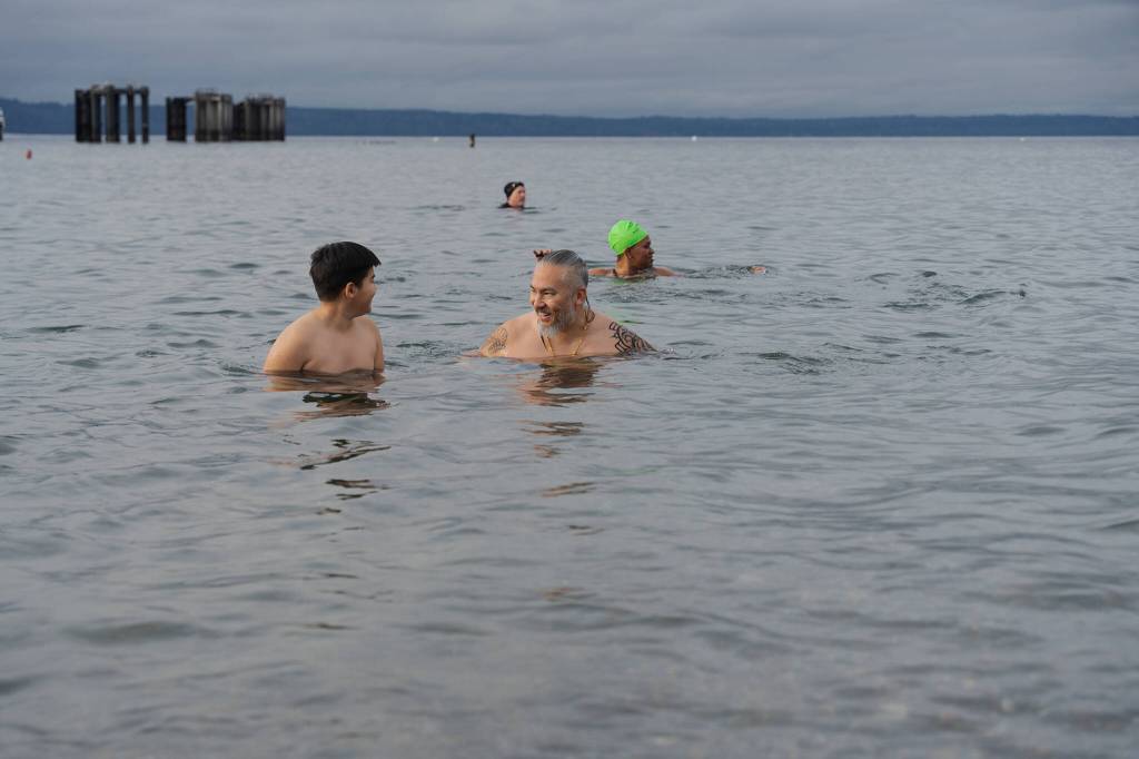 Chris Oliver, center, looks at his 11-year-old son, Jay, as the two swim in the cold water after taking the plunge on Wednesday, Jan. 1 in Edmonds, Washington (Will Geschke / The Herald)