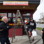 At J&L BBQ in Snohomish, owner Joel Sexton (left) talks with customer Tony Cecsarini and Austin Eisenhuth (right) after hanging banners announcing the restaurants ability to accept takeout orders. (Andy Bronson / The Herald)