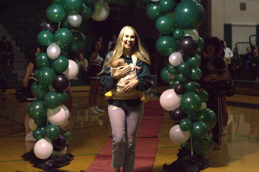 Kristi Kingma, carrying one of her children, walks through the balloon arch at an Athletic Hall of Fame ceremony at Jackson High School in Mill Creek on Jan. 17. (Aaron Coe / The Herald)