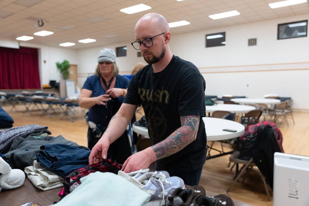 Adam Kartak helps set out donated clothing on at the east Everett cold weather shelter on Tuesday, Feb. 11 in Everett, Washington. (Will Geschke / The Herald)