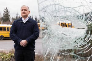 Northshore School District bus driver Stewart O’Leary pictured next to his buses shattered drivers side windshield on Friday, Feb. 14, 2025 in Bothell, Washington. (Olivia Vanni / The Herald)