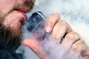 FILE - In this Friday, Oct. 4, 2019, file photo, a man using an electronic cigarette exhales in Mayfield Heights, Ohio. On Tuesday, Nov. 19, 2019, the American Medical Association said it is calling for an immediate ban on all electronic cigarette and vaping devices. (AP Photo/Tony Dejak, File)