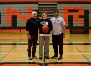 Monroe junior Tate Hammerquist stands between his grandfather, Martin (left), and father, Trevor (right), in the Monroe High School gymnasium in Monroe, Washington on Feb. 25, 2025. All three played for the Bearcats while they were in high school, as well as Tate's great-grandfather, Stan, who helped Monroe win the 1953 State Championship. (Joe Pohoryles / The Herald)