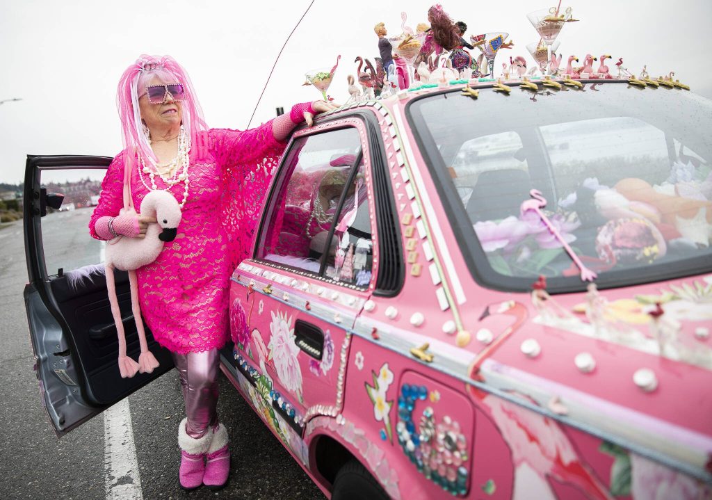 Marty Vale, a car artist, stands next to her hot pink and trinket-covered 1991 Toyota Corolla that draws attention wherever she goes. Vale, 76, of Lynnwood, also joins other cartists at parades and art shows. This is her third art car. (Olivia Vanni / The Herald)