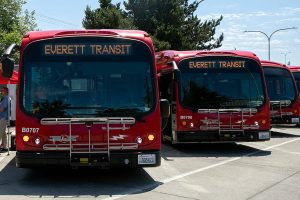 Officials gather near two of Everett’s electric buses to discuss the new BattGenie system on Monday, June 27, 2022, at the Everett Transit bus yard in Everett, Washington. (Ryan Berry / The Herald)