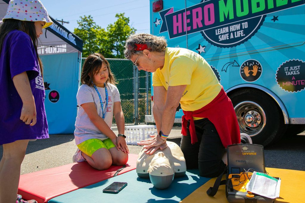 Sue Apodaca, right, shows 10-year-old Phoebe Li how to perform CPR and use an Automated External Defribrillator (AED) during the Robert C. Polk Heart Healthy Education Event on Saturday, June 3, 2023, at Memorial Stadium in Everett, Washington. Apodaca’s sister, Darla Varrenti, started the Nick of Time Foundation after the unexpected death of her teenage son, Nick Varrenti, in 2004. The organization promotes cardiac education and puts on heart screenings at high schools across the state. (Ryan Berry / The Herald)