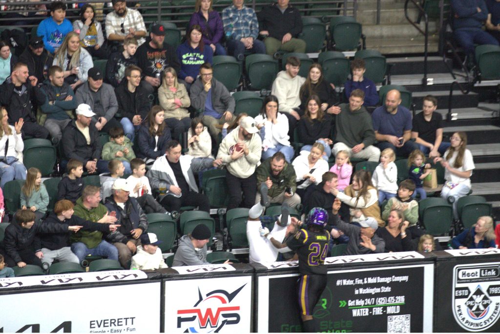 Wolfpack defensive back Armand Childs (24) tackles a Southwest Kansas player over the wall as a fan catches a football during Washington Wolfpacks 63-33 loss at Angel of the Winds Arena on March 16, 2025. (Aaron Coe / The Herald)