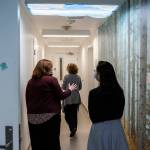 Dr. Katie Gilligan walks down a hallway with forest wallpaper and cloud light shades in the Mukilteo Evaluation and Treatment Center with Amanda Gian, right, and Alison Haddock, left, on Monday, March 24, 2025 in Mukilteo, Washington. (Olivia Vanni / The Herald)
