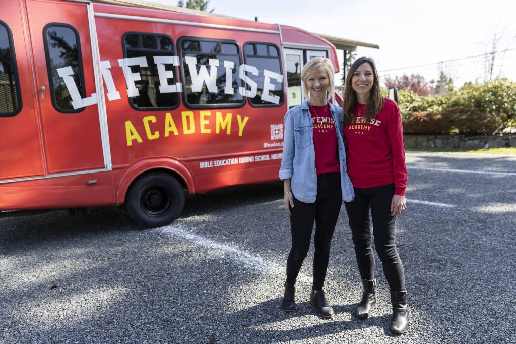 LifeWise local co-directors Darcie Hammer and Sarah Sweeny next to their student shuttle bus outside of New Hope Assembly on Monday, April 14, 2025 in Everett, Washington. (Olivia Vanni / The Herald)