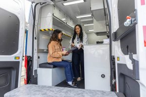 Pia Sampaga-Khim, right, and Jana Rafi, left, demonstrate how a patient check in might go in the Snohomish County Health Department’s new Health on Wheels Van on Wednesday, April 9, 2025 in Everett, Washington. (Olivia Vanni / The Herald)