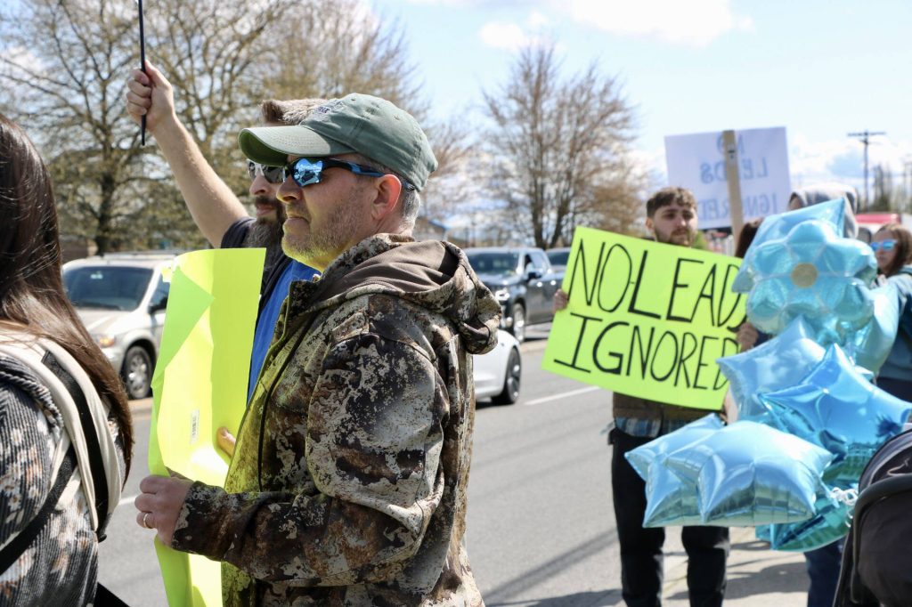 A protester holds a sign reading No Leads Ignored among a cluster of blue balloons during a call to action Saturday in Arlington. (Aspen Anderson / The Herald)