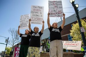 Nathan Rosas, 13, right, Avryan Flores, 16, center, and Angela Rosas, 16, hold signs in protest of a gun show at Angel of the Winds Arena ballroom on Saturday, April 29, 2023 in Everett, Washington. (Olivia Vanni / The Herald)