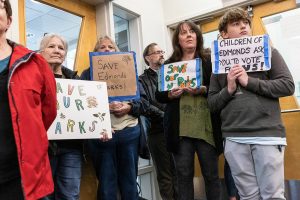 Sue Garton, left to right, Bonny McMahon, Kassie Goforth and Jack Perry stand in the Edmonds City Council chambers holding signs in protest of the city parks being considered for sale on Monday, April 21, 2025 in Edmonds, Washington. (Olivia Vanni / The Herald)