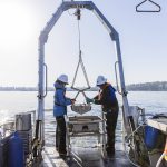 Dany Burgess, left, and Chad Eshelman, right, help maneuver their equipment holding a sediment sample up and onto the boat on Thursday, May 1, 2025 in Everett, Washington. (Olivia Vanni / The Herald)
